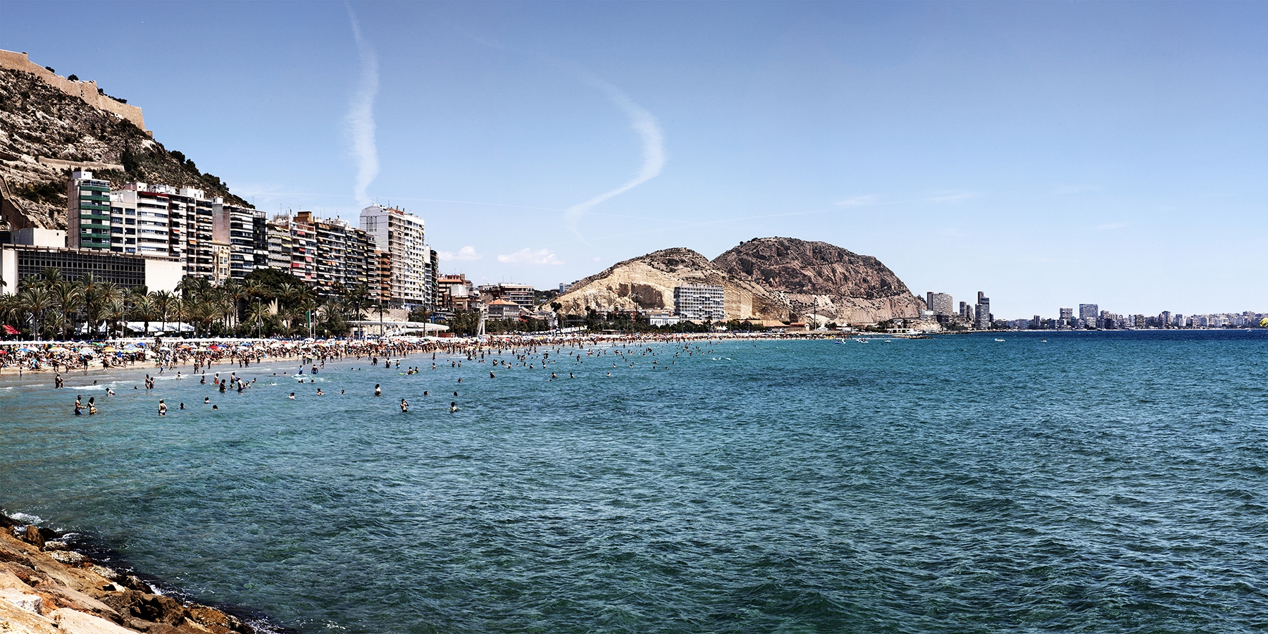 Des del moll de Llevant s’observa la platja del Postiguet plena de banyistes i, al fons, el barri del cap de l’Horta.